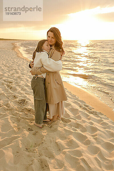 Lächelnde Frau umarmt Mädchen am Strand
