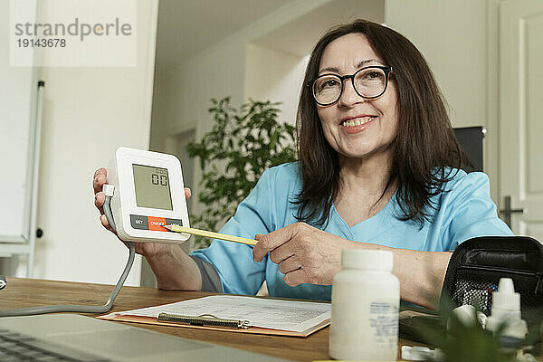 Lächelnder Arzt zeigt digitale Anzeige des Blutdruckmessgeräts