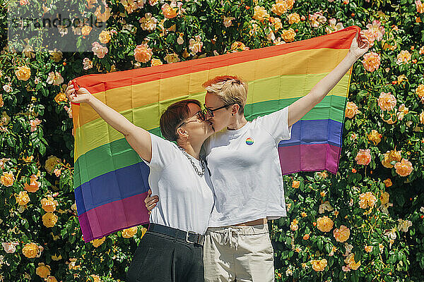 Lesbisches Paar küsst sich und hält Regenbogenfahne in der Hand