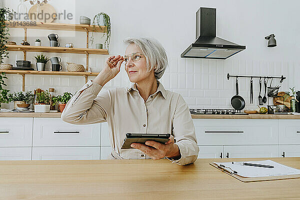 Nachdenkliche Frau mit Tablet-PC in der heimischen Küche