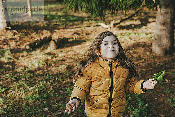 Playful girl holding nuts and fern in forest