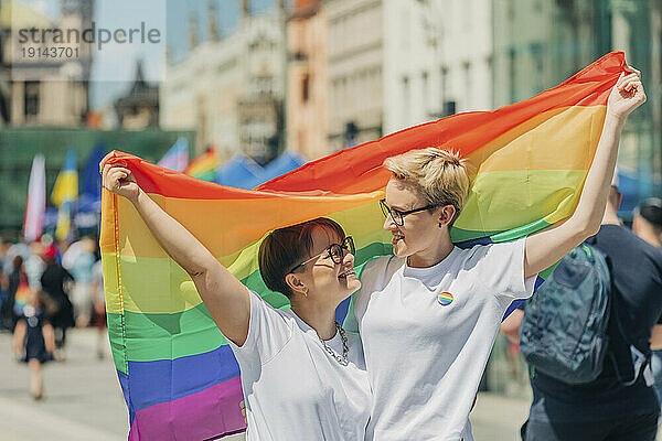 Glückliches lesbisches Paar mit Regenbogenfahne an einem sonnigen Tag