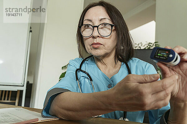 Arzt mit Brille zeigt Pulsoximeter in Arztpraxis