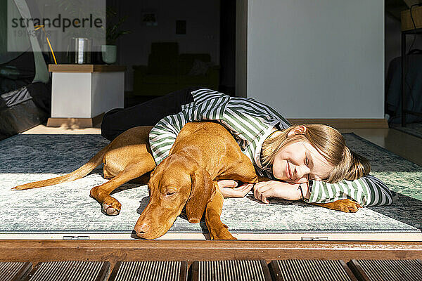 Smiling girl with Vizsla dog relaxing in sunlight at home