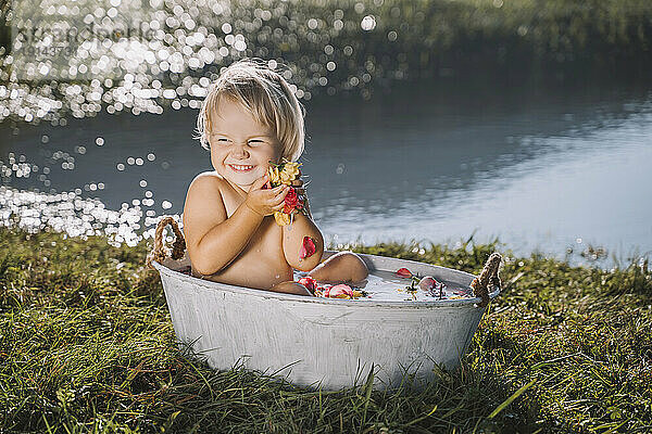 Fröhliches Mädchen hält Blumen in der Badewanne am See
