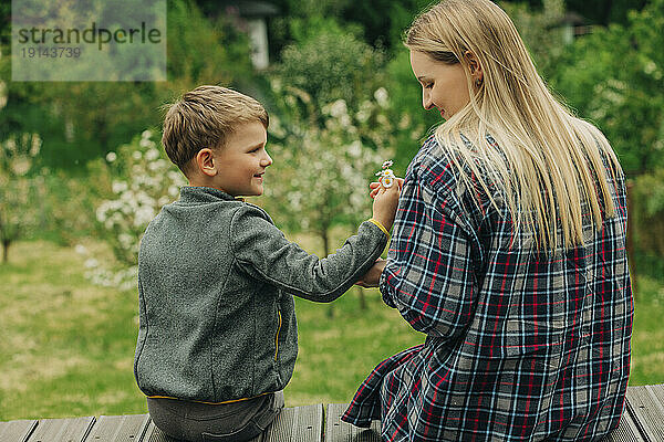 Glücklicher Sohn schenkt der im Garten sitzenden Mutter Blumen