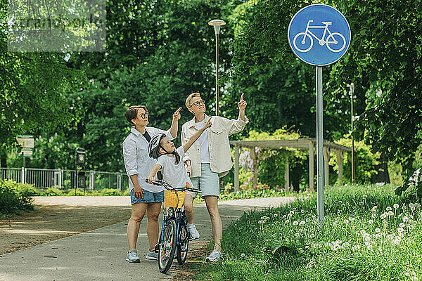 Lesbisches Paar mit Tochter zeigt auf Fahrradwegschild im Park