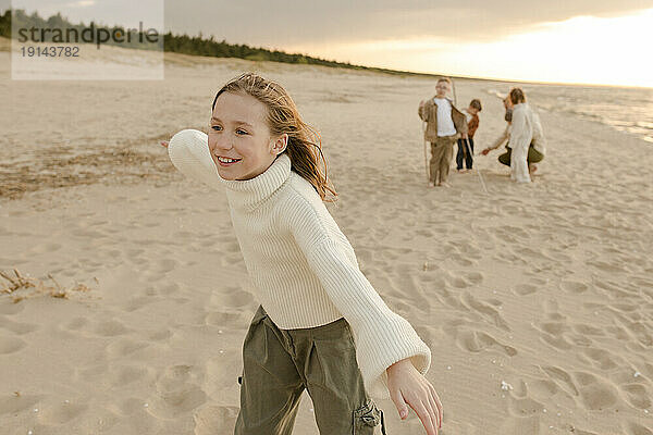 Lächelndes Mädchen  das am Strand spielt  mit der Familie im Hintergrund