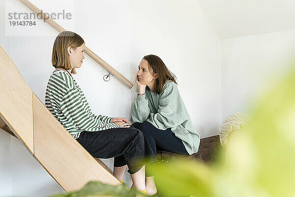 Tochter spricht mit Mutter  die zu Hause neben der Treppe sitzt