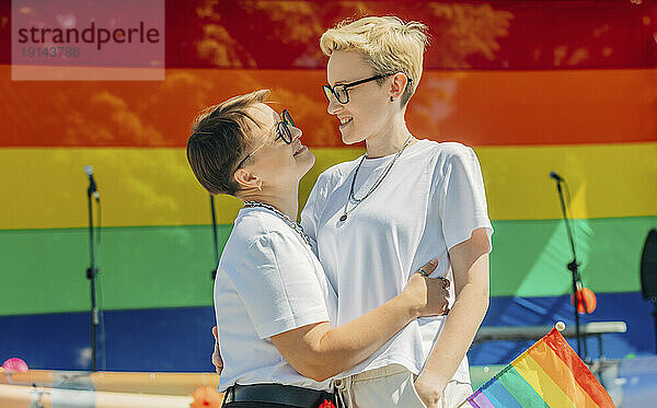 Fröhliche Lesben umarmen sich vor der Regenbogenfahne