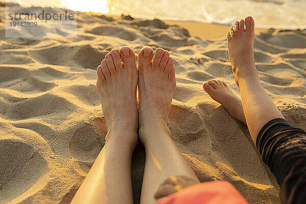 Mutter und Tochter entspannen sich barfuß im Sand am Strand