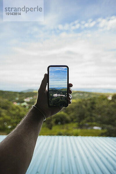 Hand of man clicking photograph of nature through smart phone