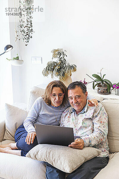 Älteres Paar teilt sich Laptop und sitzt zu Hause auf dem Sofa
