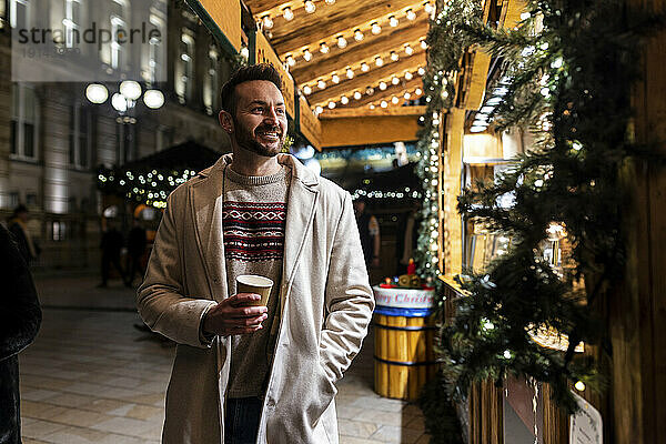 Mann mit Kaffeetasse steht auf dem Weihnachtsmarkt