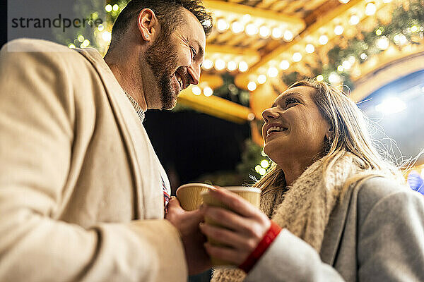 Lächelnde Männer und Frauen genießen Kaffee auf dem Weihnachtsmarkt