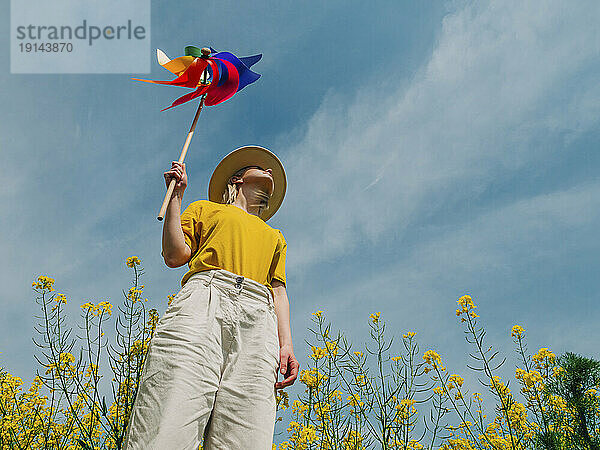 Frau hält Windradspielzeug im Rapsfeld unter freiem Himmel