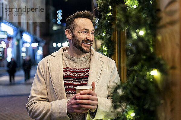 Glücklicher Mann steht mit Kaffeetasse auf dem Weihnachtsmarkt