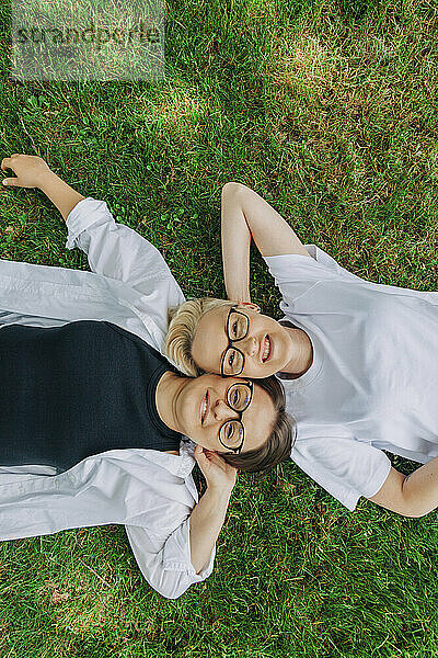 Lächelndes lesbisches Paar mit den Händen hinter dem Kopf im Gras liegend