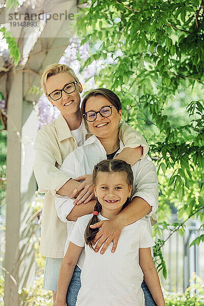 Smiling lesbian couple with daughter standing with arms around at park