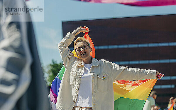 Fröhliche lesbische Frau mit Regenbogenfahne genießt die Gay-Pride-Veranstaltung