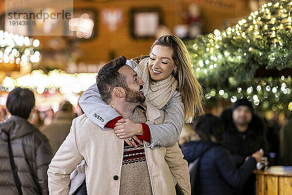 Happy man giving piggyback ride to woman at Christmas market