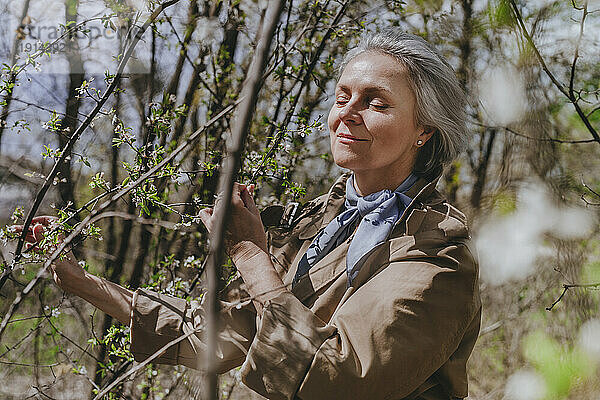 Frau mit geschlossenen Augen riecht Blumen im Wald