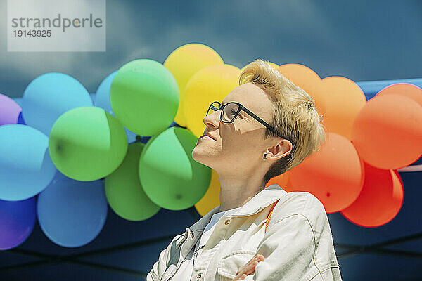 Blonde Frau mit Brille vor regenbogenfarbenen Luftballons