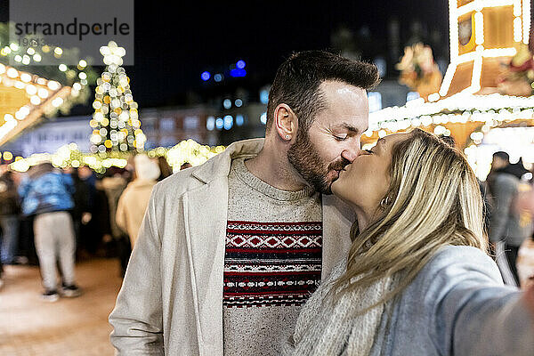 Junge Frau und Mann küssen sich auf dem Weihnachtsmarkt