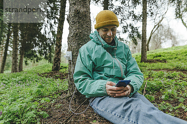 Mann lädt Smartphone mit Steckdose am Baumstamm auf