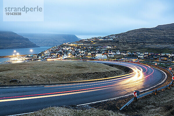 Leichte Wanderwege auf der Straße mit der Stadt Eidi im Hintergrund in der Abenddämmerung  Färöer-Inseln