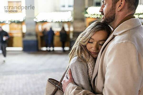 Junge Frau umarmt Mann auf Weihnachtsmarkt