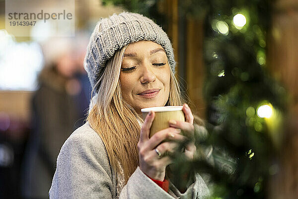 Lächelnde Frau hält Kaffeetasse auf dem Weihnachtsmarkt