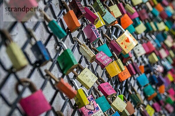 Bunte Vorhängeschlösser mit eingravierten Namen und Daten stehen für Liebe auf einem Zaun