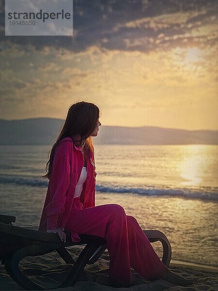 Sorglose junge Frau ästhetisches Porträt sitzen entspannt auf der Sonnenliege am Strand mit Blick auf den Sonnenaufgang über dem Meer. Wunderschöne Szene der Morgendämmerung am Meer. Sommerurlaub  Reisen und Entspannung Konzept