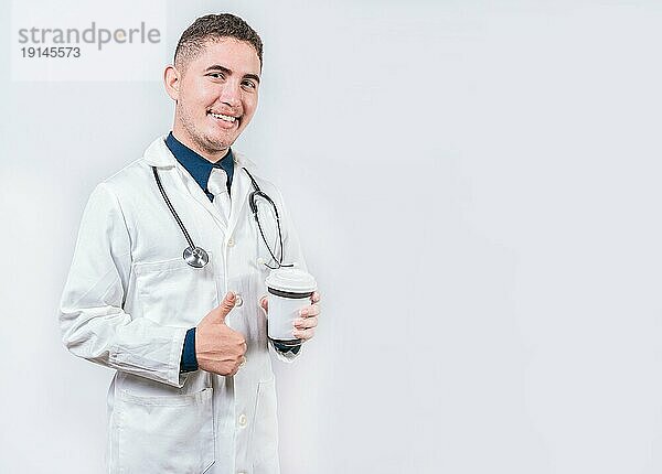 Zufriedener Arzt mit Kaffee zum Mitnehmen isoliert. Junger Arzt hält einen Kaffee zum Mitnehmen isoliert. Lächelnder Arzt hält Kaffee mit Daumen nach oben