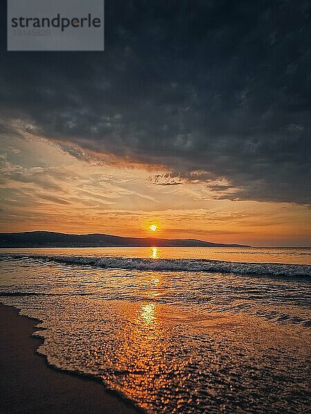 Ruhiger Morgen am Meer mit schönem Sonnenaufgang am Horizont und schäumenden Wellen auf dem Sandstrand