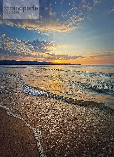 Lebhafter Sonnenaufgang am Meer mit schäumenden Wellen  die den Sandstrand umspülen. Morgendämmerung Szene mit der Sonne steigt die Hügel am Horizont