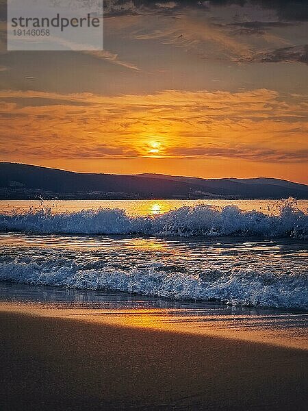 Ein Morgen am Meer mit einem strahlenden Sonnenaufgang am Horizont und schäumenden Wellen  die auf den Sandstrand schlagen