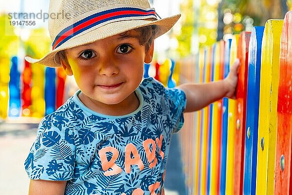 Porträt eines fröhlichen Jungen mit Hut  der auf einem Spielplatz spielt und in die Kamera schaut