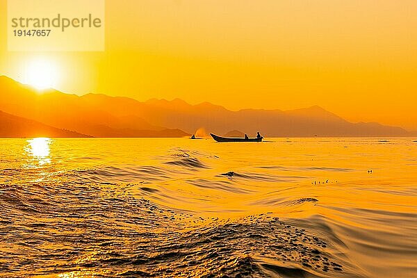 Silhouette eines Fischerboots mit einem Fischer beim Fischen im orangefarbenen Sonnenuntergang auf dem Shkoder See in Shiroka. Albanien