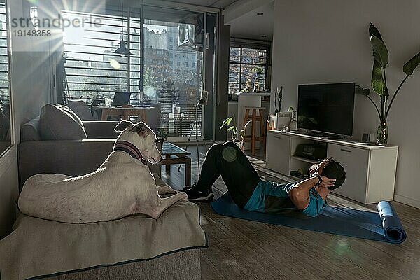 Ein fitter Mann trainiert zu Hause mit seinem Hund. Mit Sonnenstrahlen beleuchtete Umgebung