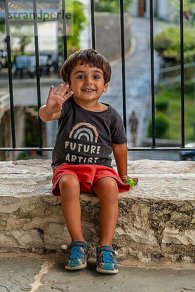 Porträt eines zweijährigen Jungen  der sehr fröhlich sitzt und die Sommerferien genießt