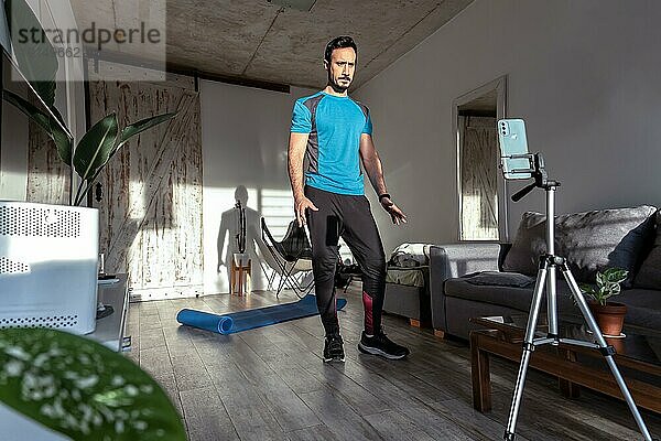 Lateinischer männlicher Trainer  der mit dem Telefon zu Hause Online Workout streamt. Online Fitnessstudio Klasse