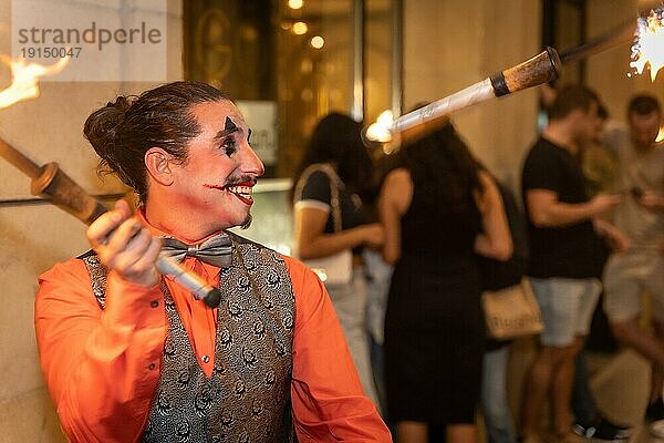 Lächelnder Jongleur auf einer Halloweenparty der mit Stöcken und Feuer jongliert  am Eingang des Nachtclubs