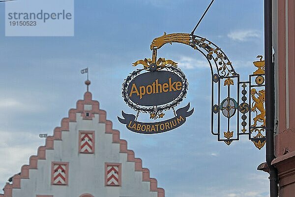 Nasenschild der Hofapotheke mit goldener Inschrift Laboratorium und unschärfe Stufengiebel vom Rathaus  Tiefenunschärfe  Kunsthandwerk  Löwenfigur  Symbol  Apotheke  Verzierung  Freisteller  Marktplatz  Bad Mergentheim  Franken  Baden-Württemberg  Deutschland  Europa