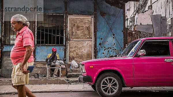 Havanna  Kuba am 23. Dezember 2015: Ein Mann geht eine Straße in Centro Habana entlang  sein Hemd hat die Farbe eines rosa Oldtimers