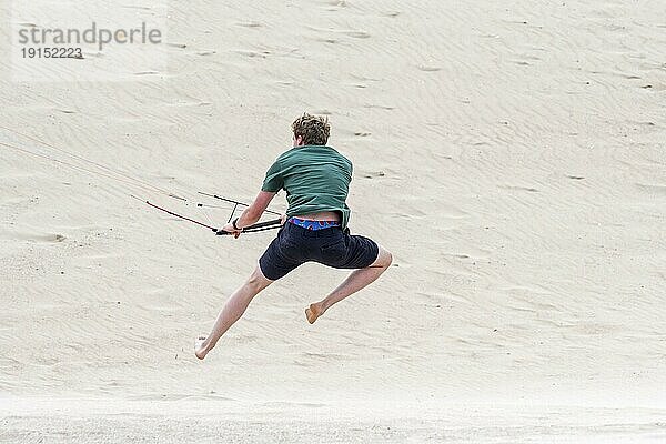 Junger Mann beim Umgang mit der 4 Leiner Bar eines fliegenden Vierleiner Trainers Parafoil  4 Leiner Lenkdrachen am Sandstrand bei starkem Wind im Sommer