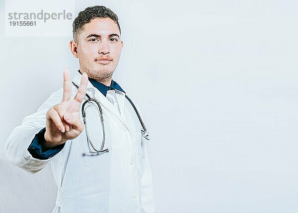 Lateinischer Arzt  der die Zahl zwei zählt  isoliert. Lächelnde junge Arzt Zählen von Nummer 2 auf isolierten Hintergrund
