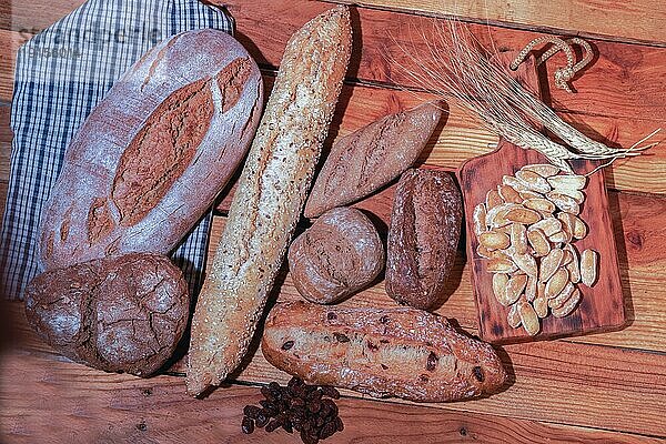 Draufsicht auf eine Auswahl rustikaler Brote aus verschiedenen Körnern und Mehlen auf einem Holztisch mit Weizenähren