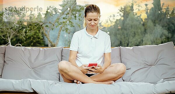 Eine Frau  die einen ruhigen Urlaub genießt  während sie sich in einer bequemen Schaukel in ihrem Garten ausruht und ihr Smartphone benutzt